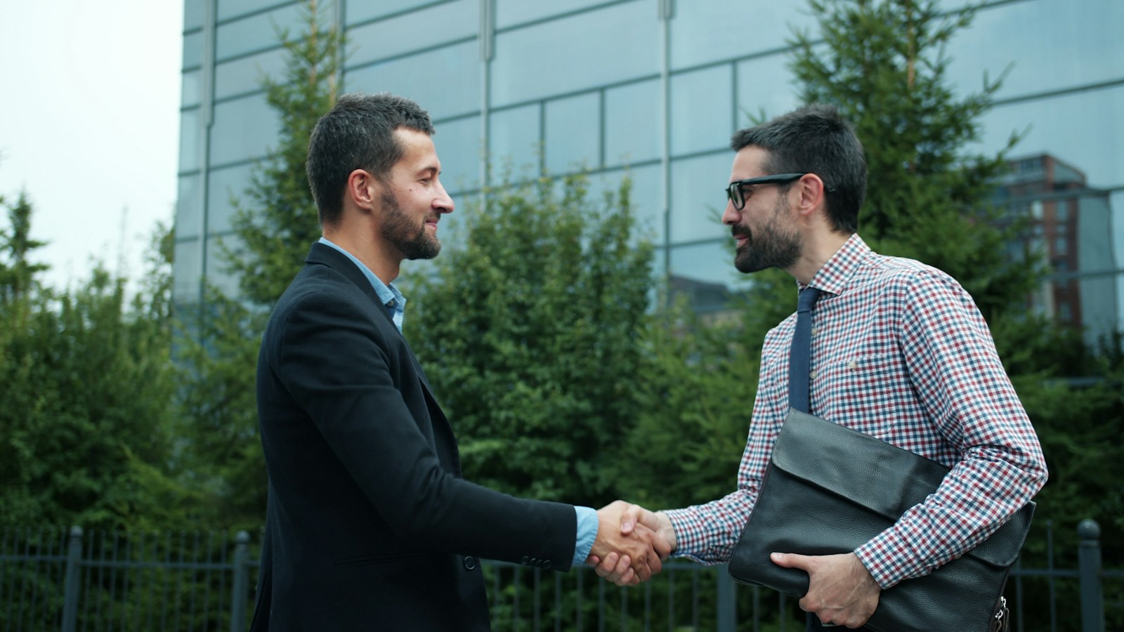 Two businessmen shaking hands outside modern building