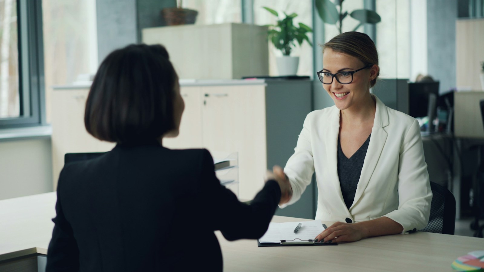 Two women shaking hands across a desk