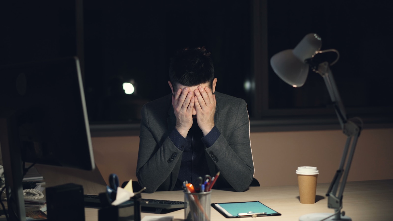 Man in suit sits at desk, head in hands