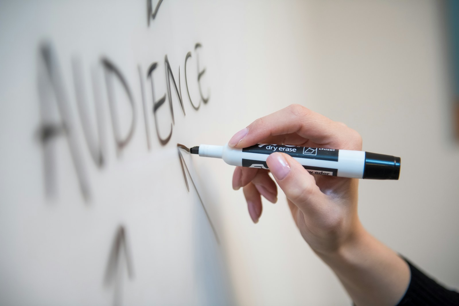 A hand holding a black dry erase marker writing on a white board