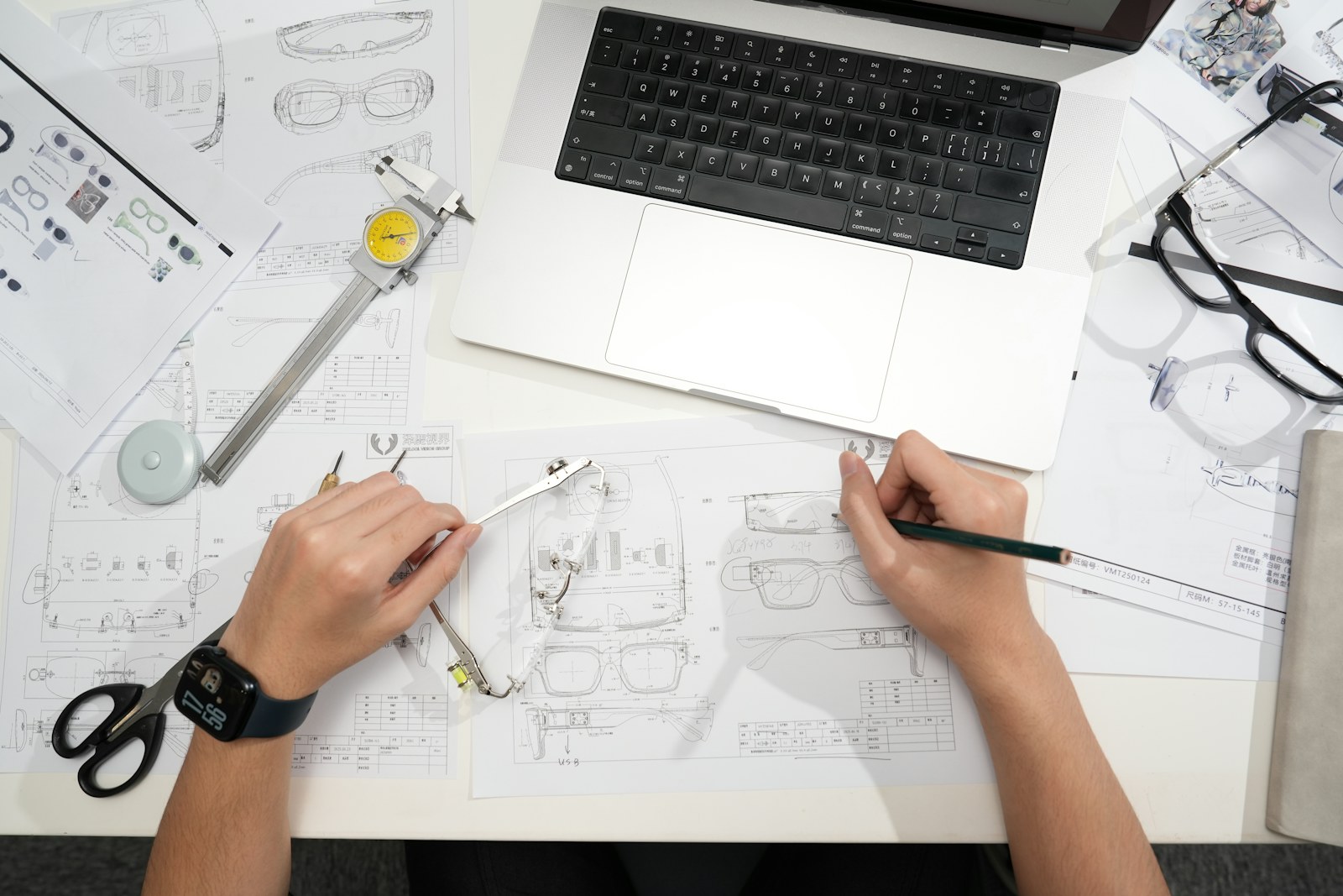 Designer sketching eyeglasses with laptop and tools