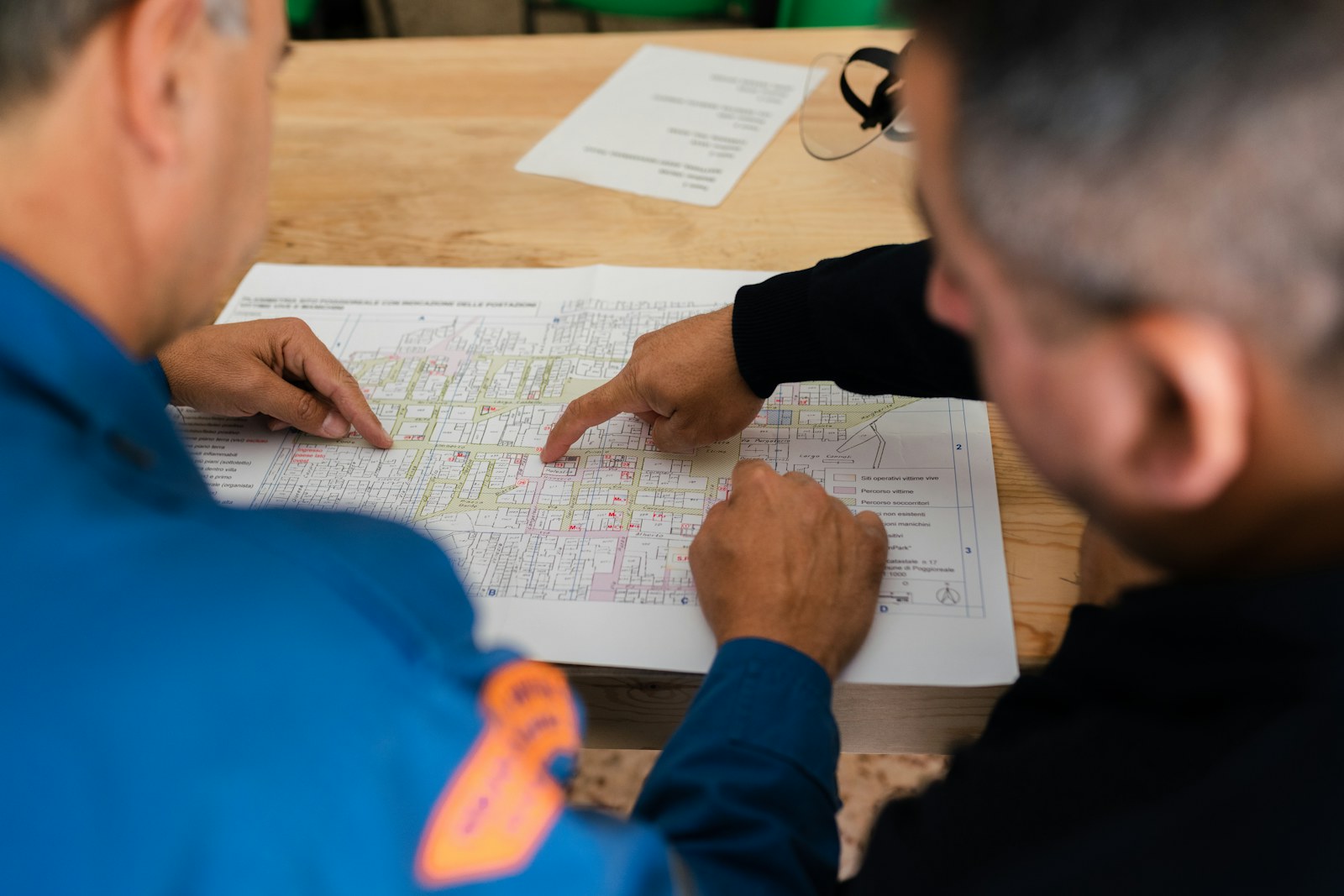 Two people in blue uniforms pointing at a printed map on a table