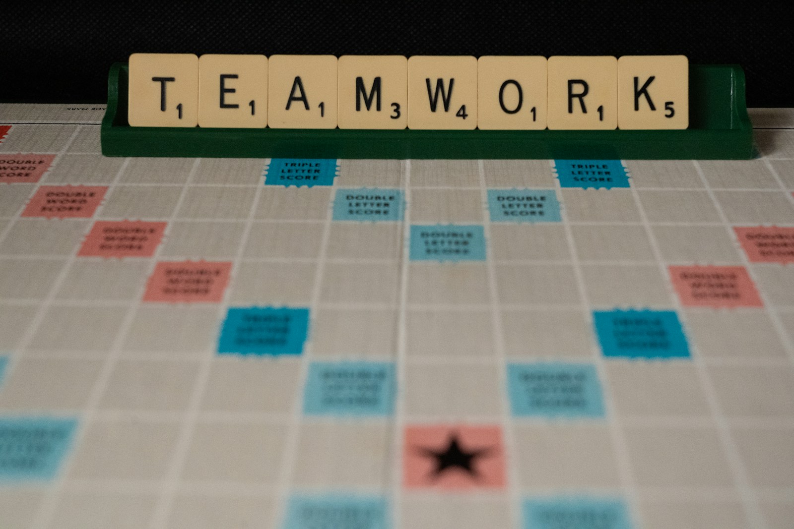 Scrabble tiles spelling teamwork on a green rack above a game board