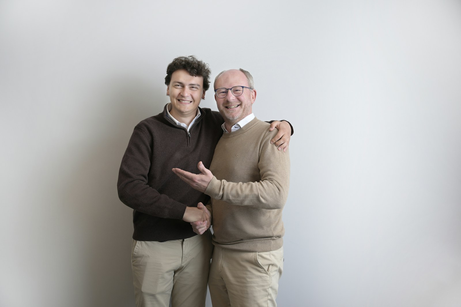 Two smiling men shaking hands against a white wall