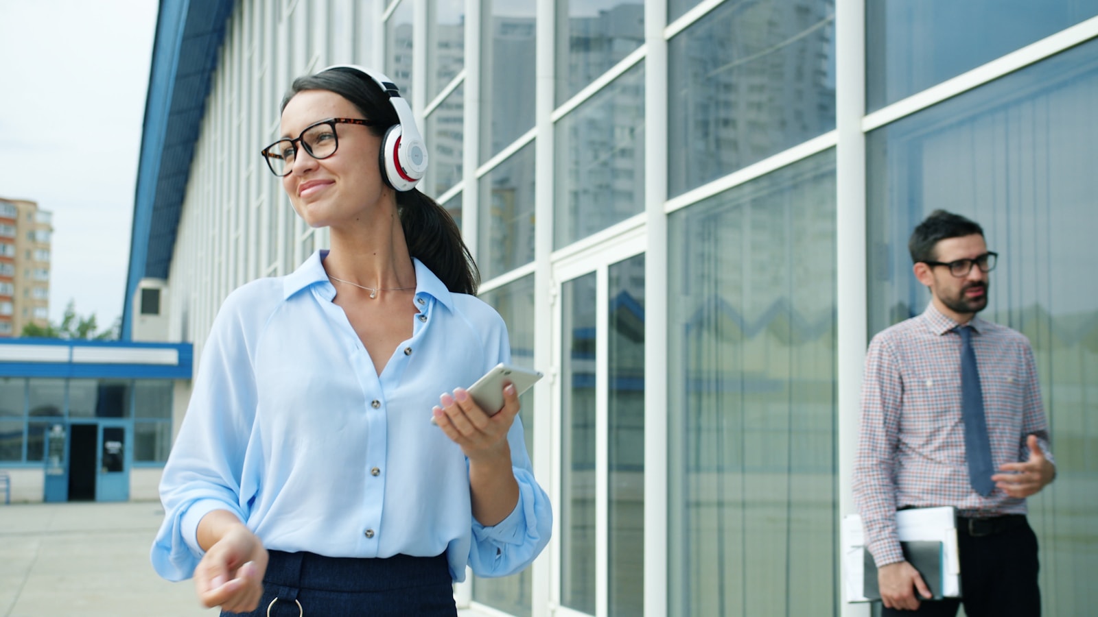 Woman with headphones walks past a man outside building