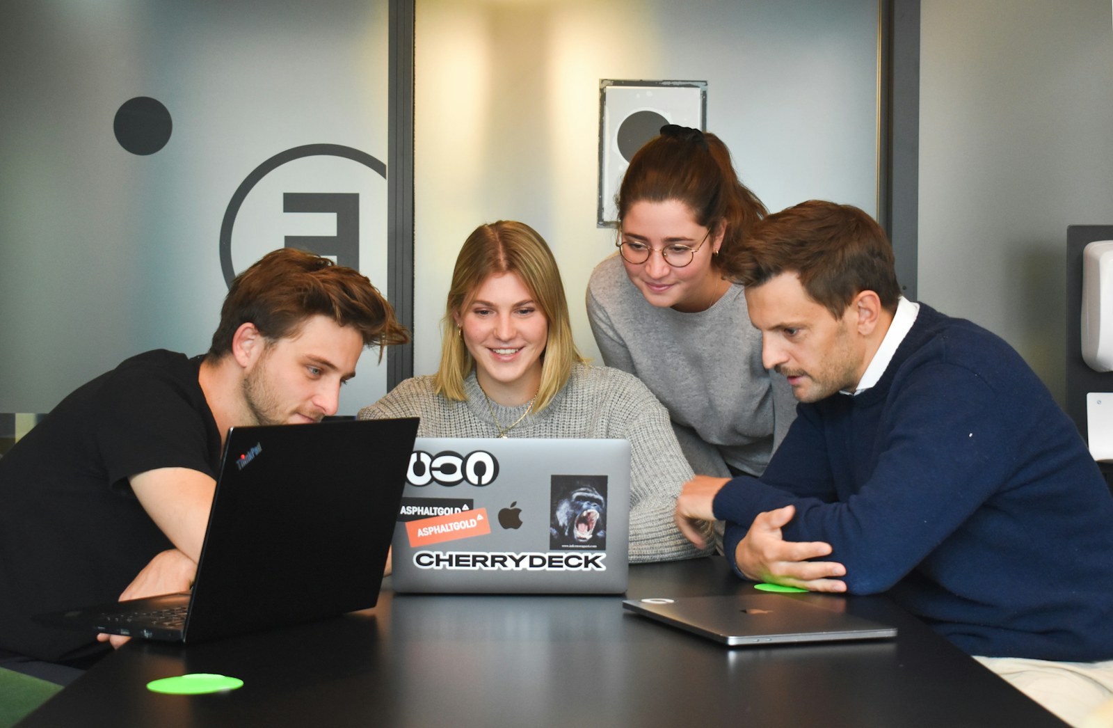 Four people collaborating around a laptop on a table in a modern office