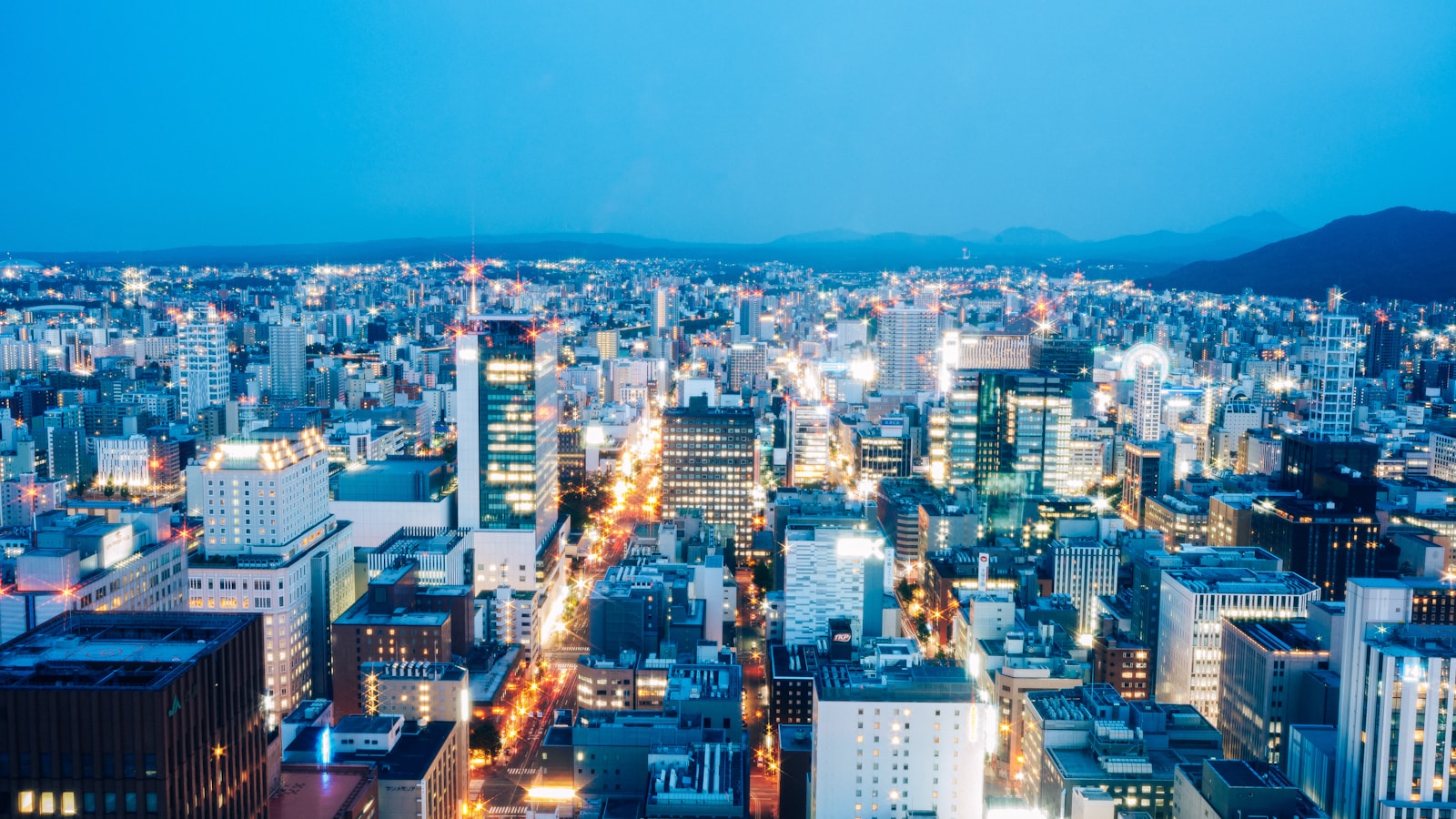 Cityscape at night with illuminated buildings and distant mountains