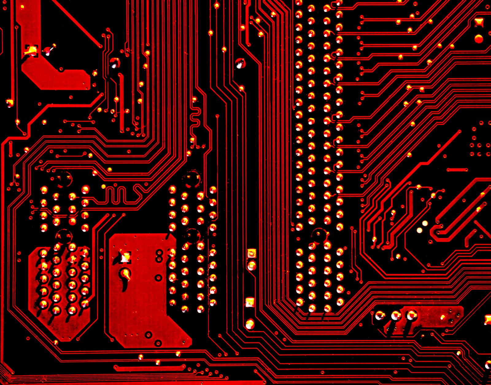 A red and black circuit board with intricate metallic pathways and solder points