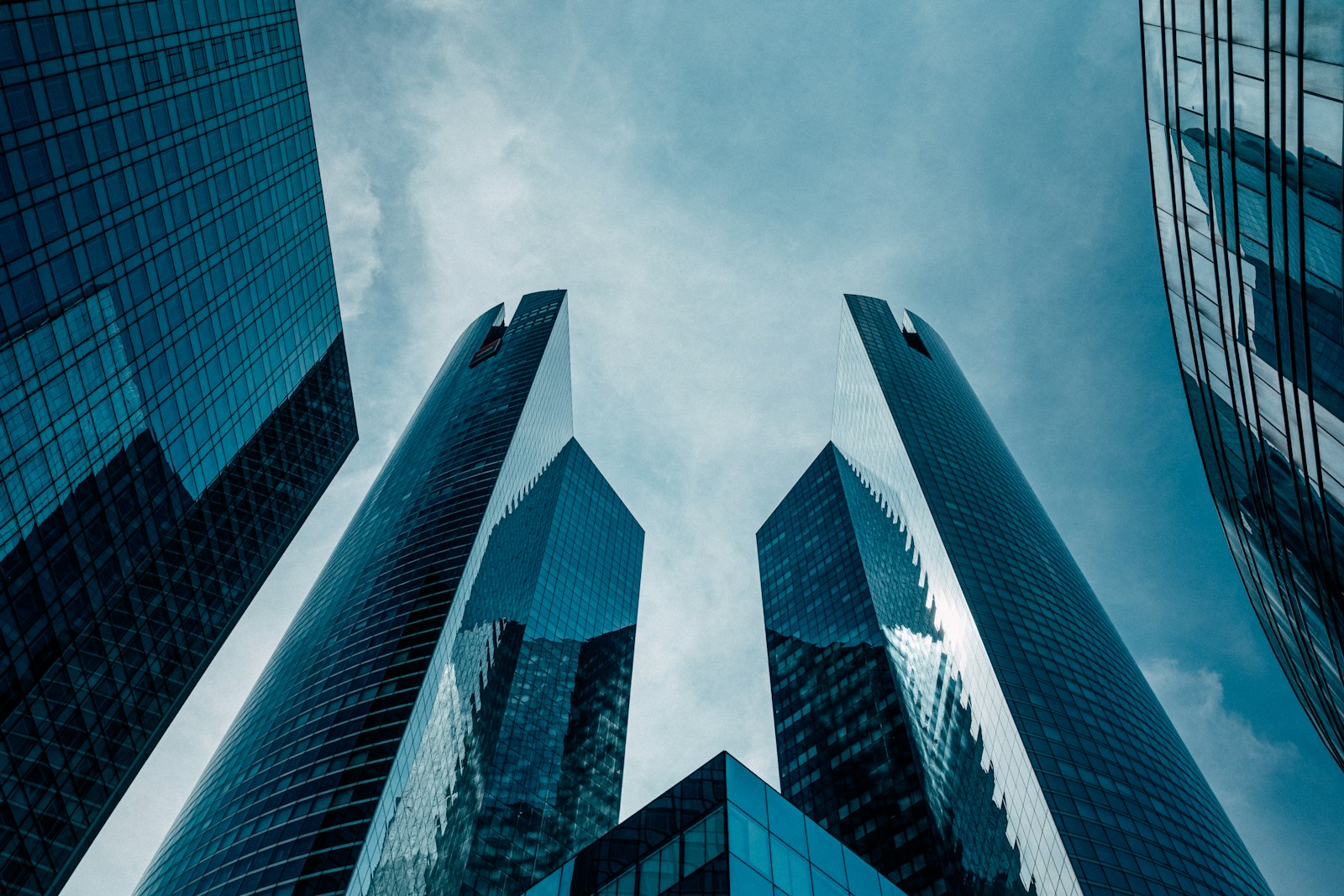 Low angle view of modern glass skyscrapers reaching toward a cloudy blue sky