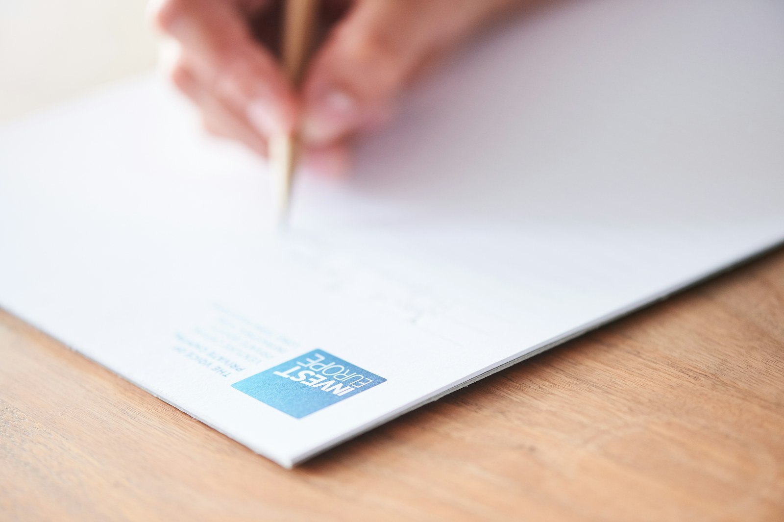 A hand writes on white paper with a blue logo