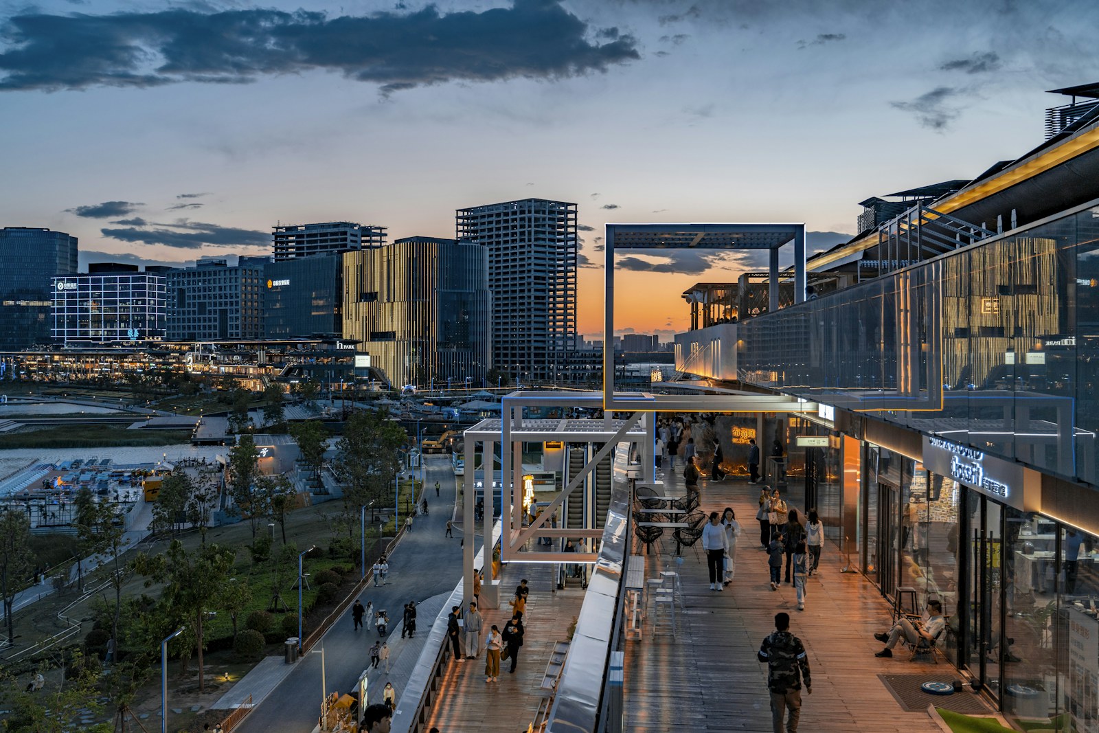 People walking on a wooden promenade beside modern buildings under a warm evening sky