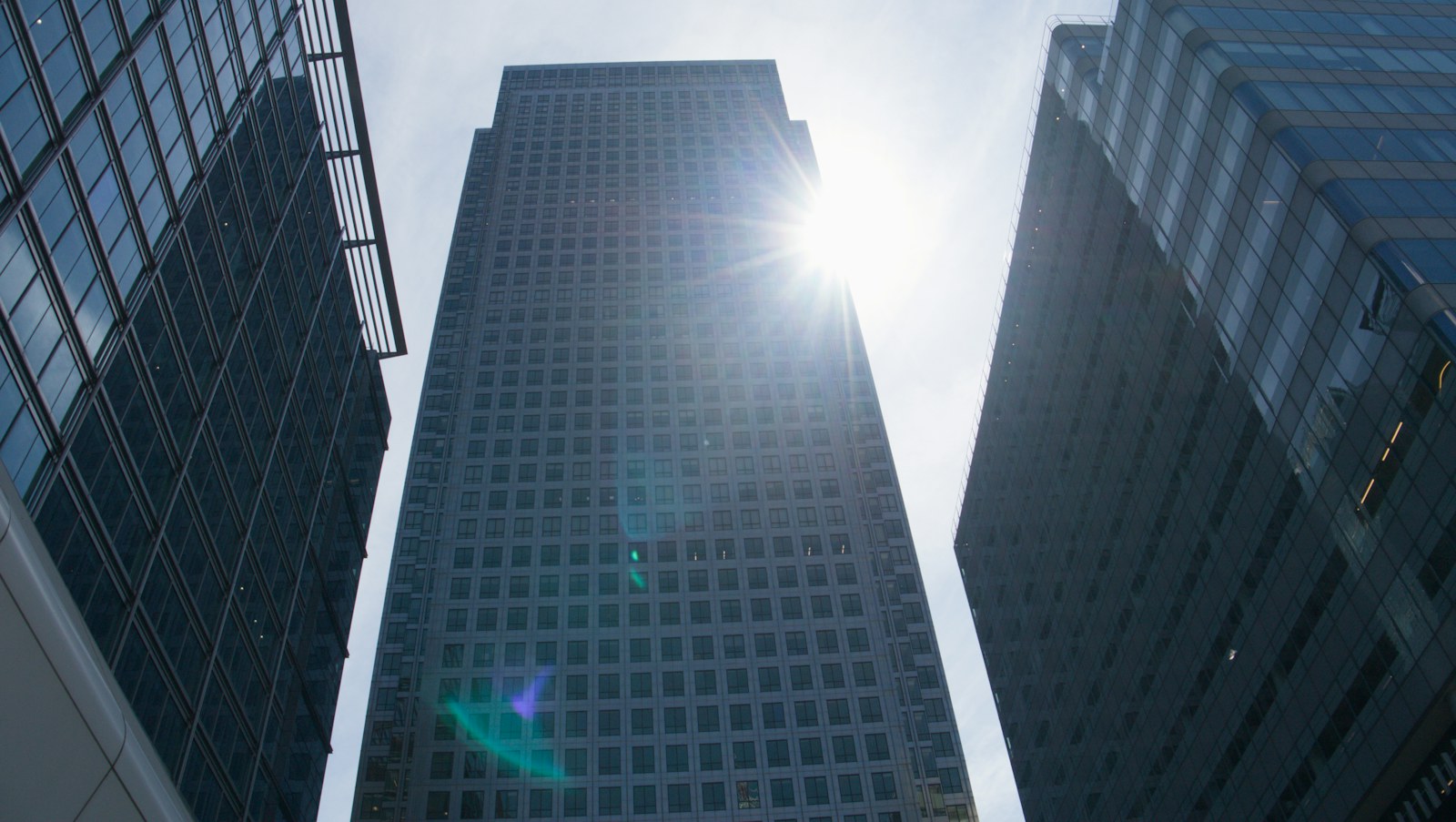 Sunlight reflects off a tall skyscraper amidst urban buildings