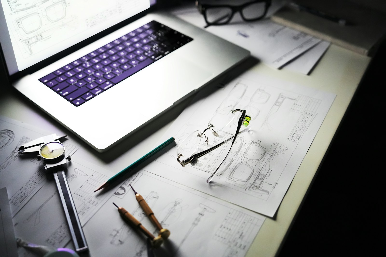 Desk with laptop, blueprints, and tools