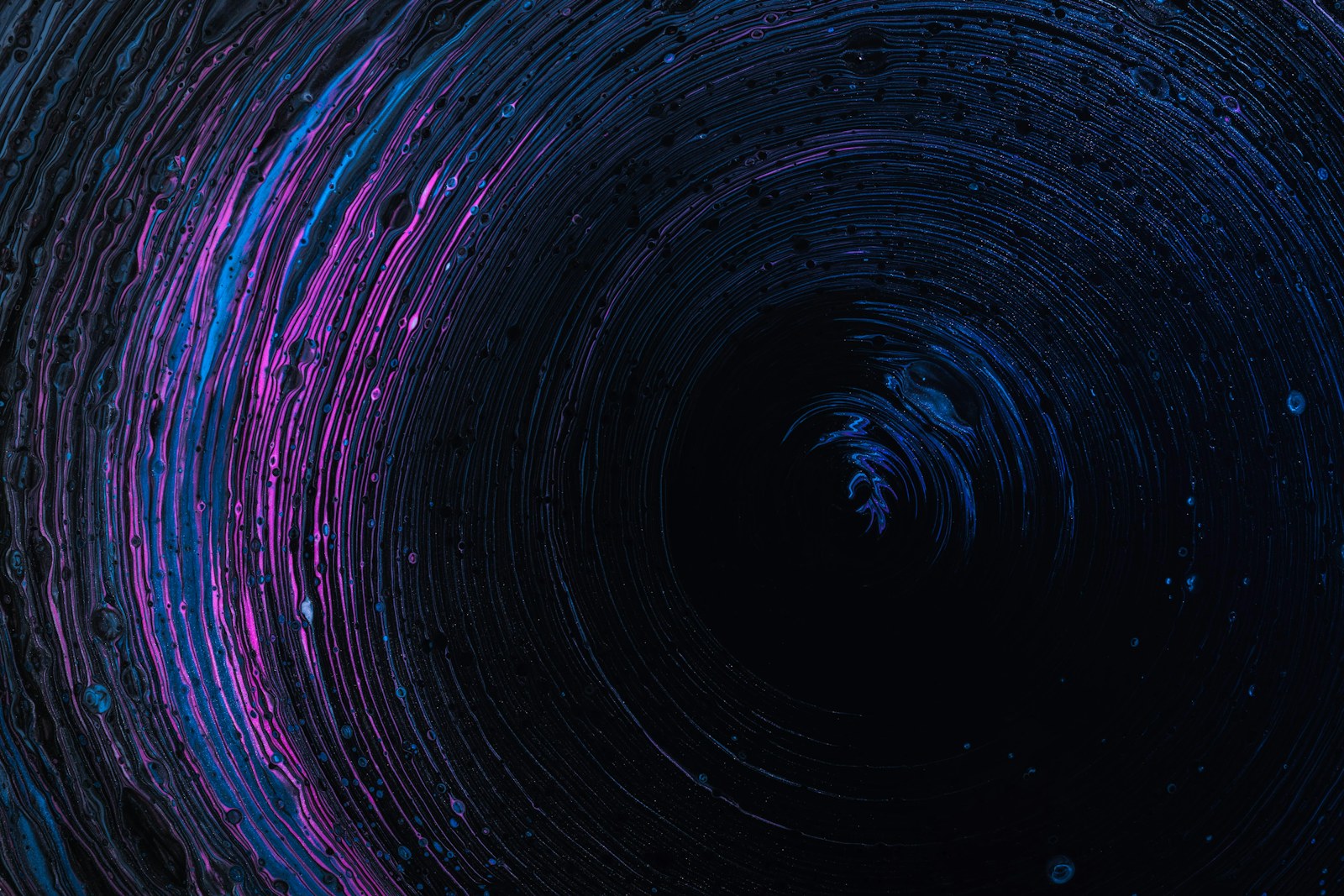 Concentric rings of blue and purple liquid paint swirling against a black background
